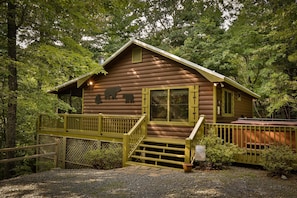 A rustic cabin with a wooden exterior, a deck, and a window with a view of the surrounding forest. - Cherry Beary Den Nevaeh Cabin Rentals (Blue Ridge)