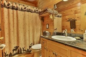 A bathroom with a wooden interior, a sink, a toilet, and a shower curtain with a forest animal print. - Cherry Beary Den Nevaeh Cabin Rentals (Blue Ridge)