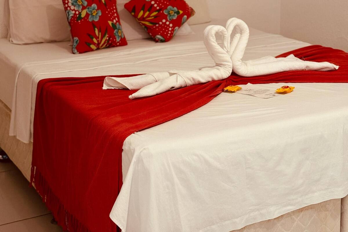 Ein Hotelzimmer mit einem Bett, roten Kissen mit Blumenmuster, einem weißen Handtuch in Form eines Schwans und einem Bild von einem Seestern an der Wand.