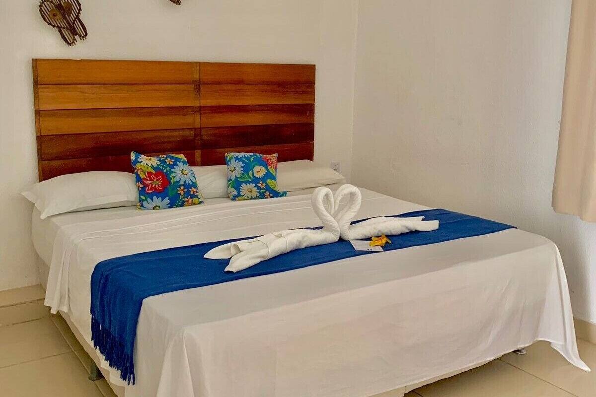 Ein ordentlich bezogenes Bett mit einer blauen Tagesdecke und einem weißen Handtuch, das zu einer Schwanform arrangiert ist.