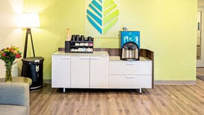 A reception area with a white counter, a coffee machine, a trash bin, and a lamp. - WoodSpring Suites Reno Sparks (Sparks)