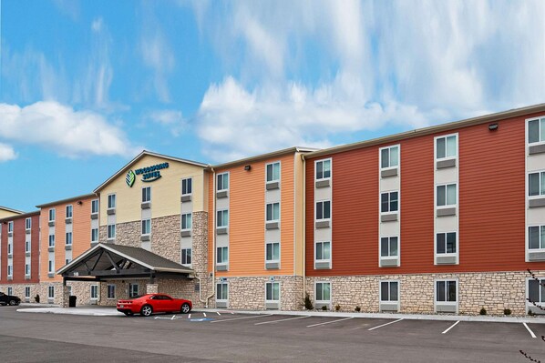 A multi-story hotel with a stone facade, a parking lot, and a red car parked in front.