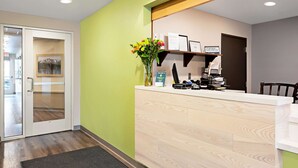 A reception area with a wooden reception desk, a vase with flowers, a welcome sign, and a door leading to another room. - WoodSpring Suites Reno Sparks (Sparks)
