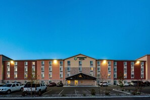 A multi-story hotel with a central entrance, parking lot, and a clear sky.
