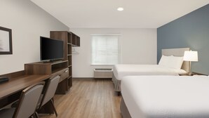 Una habitación de hotel con un escritorio de madera, televisión, cama y ventana con persianas.