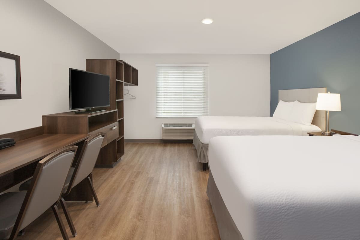 Een hotelkamer met een houten bureau, een televisie, een bed en een raam met zonwering.