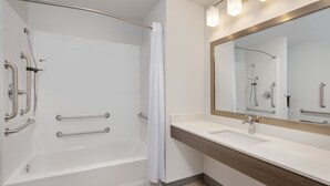 Un baño moderno con ducha a nivel, barras de apoyo, un espejo grande y un tocador con lavamanos.