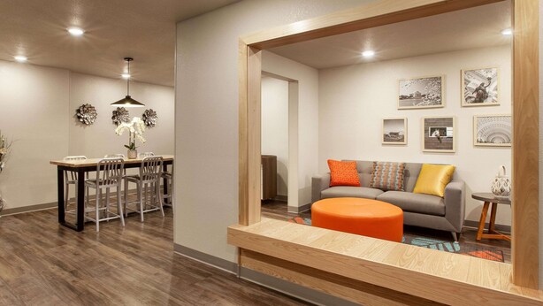 Una sala de estar moderna con una mesa de comedor de madera, sillas, un sofá con cojines de colores y un espejo que refleja la habitación.