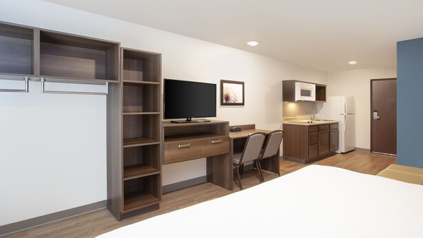 Una habitación de hotel moderna y compacta con cama, escritorio, televisor, microondas y refrigerador.