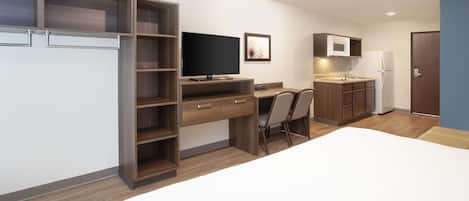 A modern, compact hotel room with a bed, a desk, a TV, a microwave, and a refrigerator.