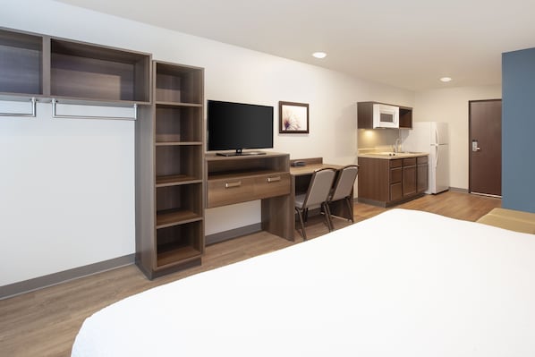 A modern, compact hotel room with a bed, a desk, a TV, a microwave, and a refrigerator. - WoodSpring Suites Washington DC Northeast Greenbelt (Greenbelt)