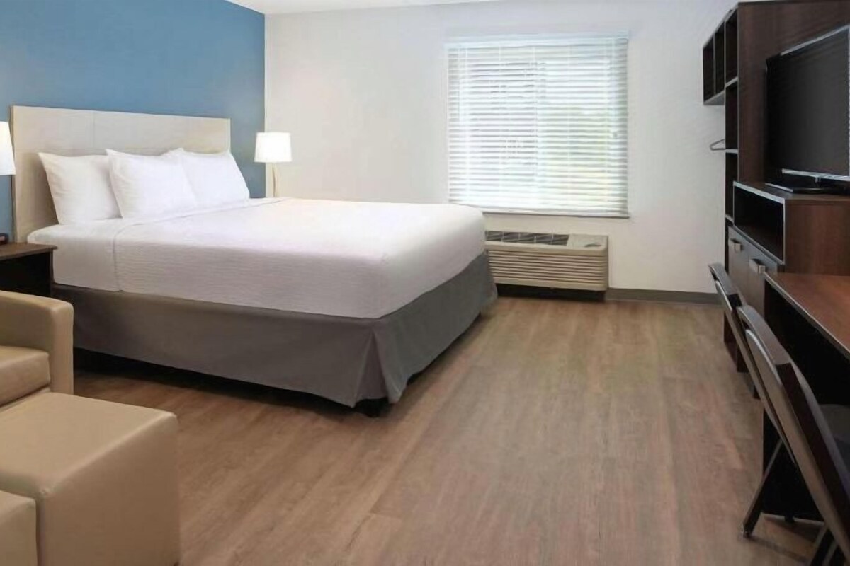 Een hotelkamer met een bed, bureau, stoel, televisie en een raam met jaloezieën.