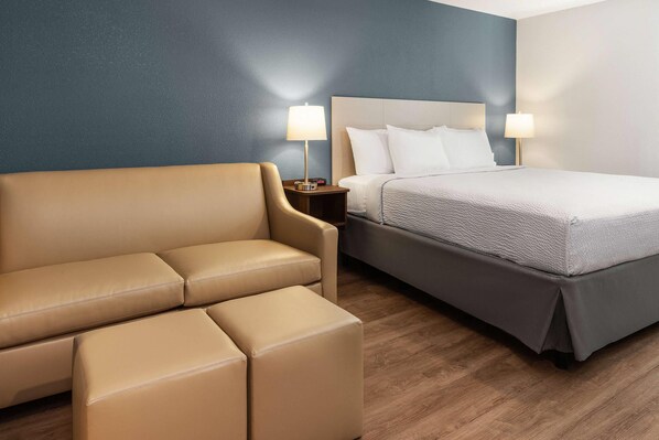 A hotel room with a bed, a sofa, two bedside lamps, and a clock on the nightstand.