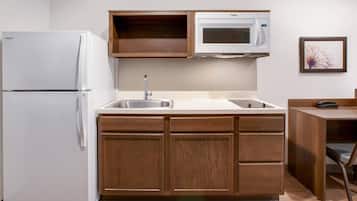 Una cocina compacta con refrigerador, microondas, lavamanos y armarios de madera.