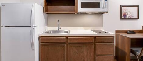 A compact kitchen with a refrigerator, microwave, sink, and wooden cabinets.