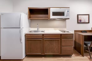 Una cocina compacta con refrigerador, microondas, lavamanos y armarios de madera.