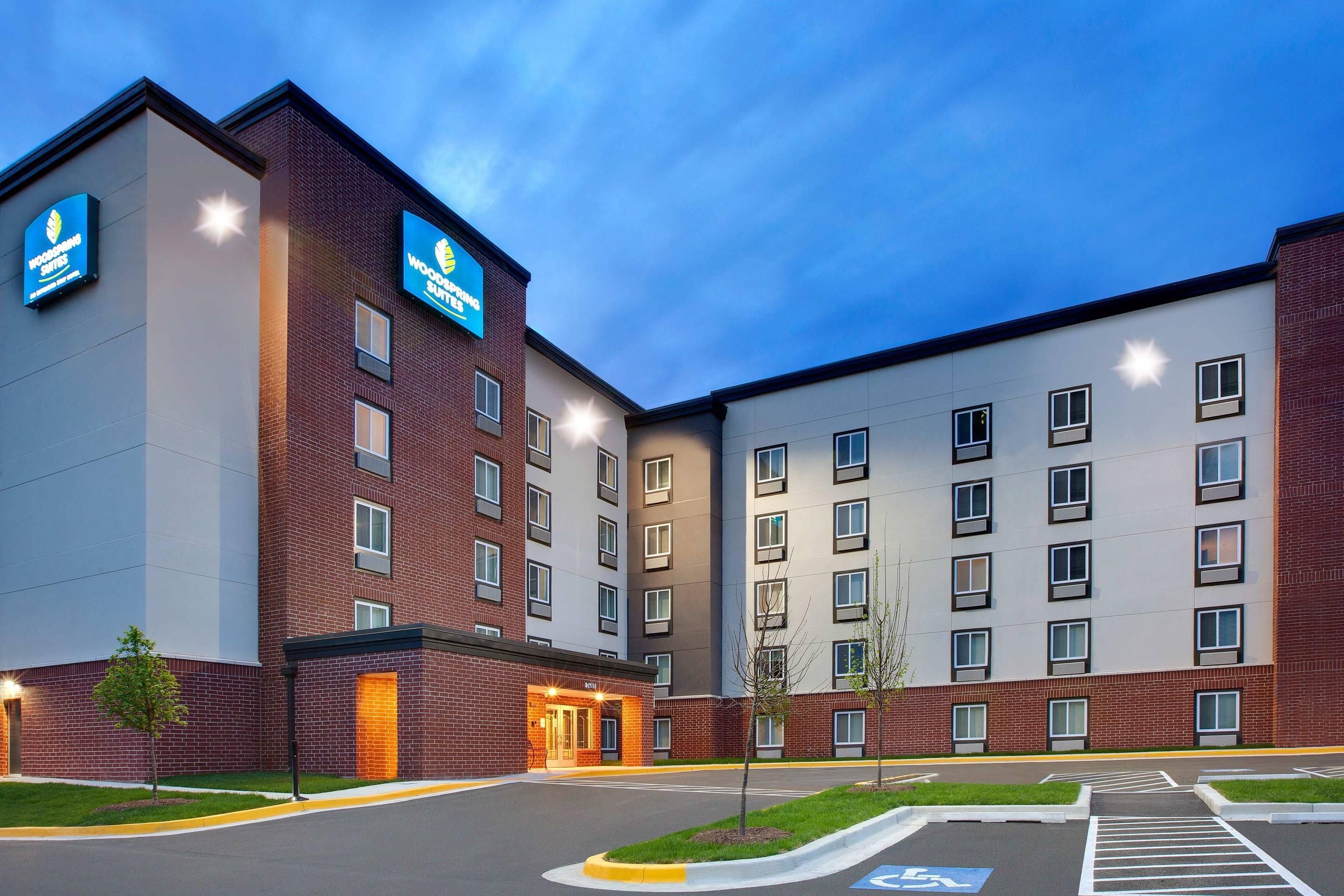 Hotel com vários andares, fachada de tijolos, entrada central e estacionamento com vagas para deficientes.