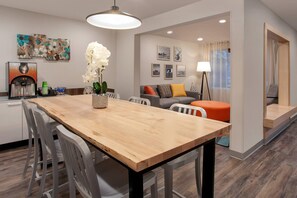 A modern living room with a wooden dining table, white chairs, a sofa, and a coffee machine.