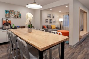 A modern living room with a wooden dining table, white chairs, a sofa, and a coffee machine.