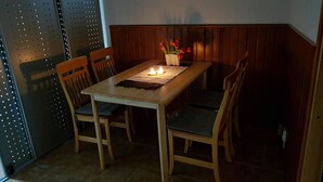 Een houten eettafel met vier stoelen, een kaars als middelpunt en een vaas met bloemen.