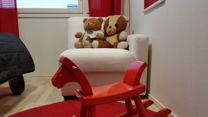 Een rood schommelpaard in een kamer met een witte fauteuil en een teddybeer erop.