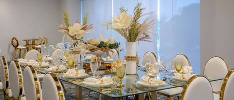 A formal dining room with a glass table, gold chairs, and white floral centerpieces.