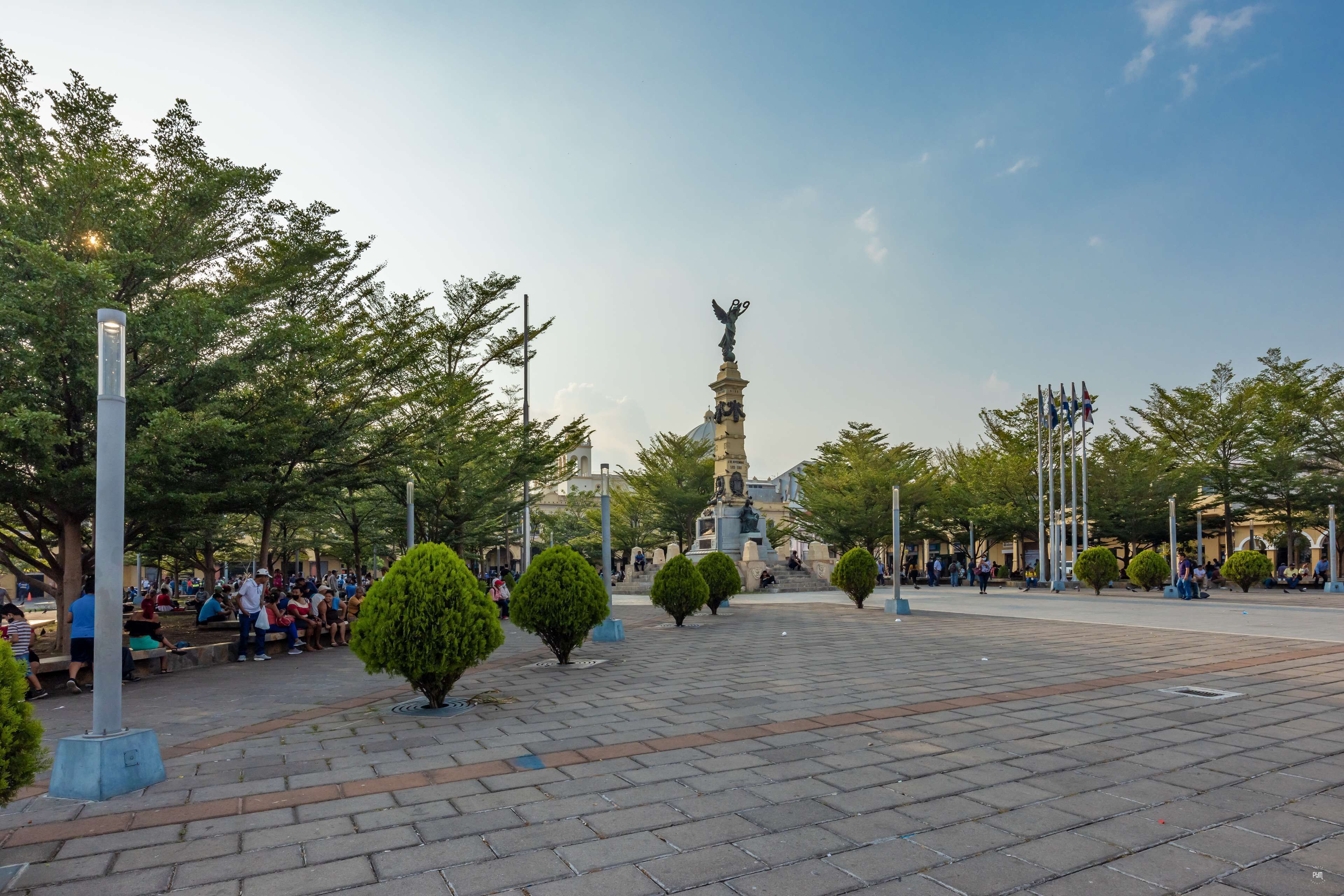 Une place publique avec un monument central, des bancs et des arbres.