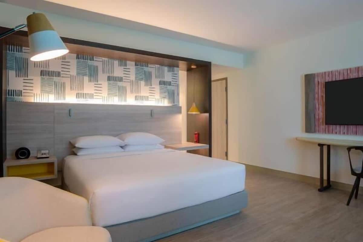 Une chambre d’hôtel moderne équipée d’un lit, d’une table de chevet, d’une lampe et d’un bureau avec une chaise.