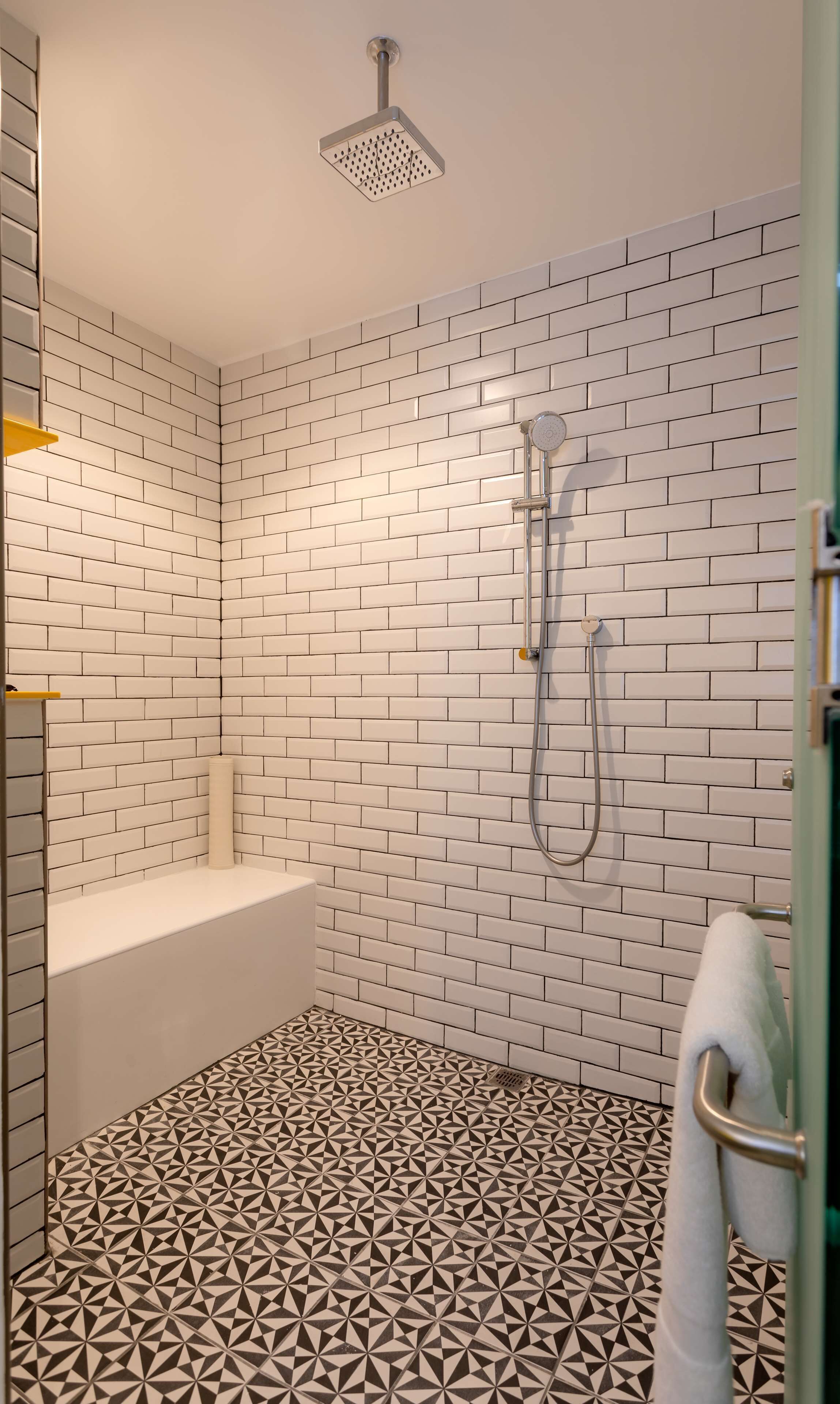 Une salle de bain avec des murs recouverts de briques blanches disposées en motif, un sol à motifs géométriques, une pomme de douche et une baignoire.