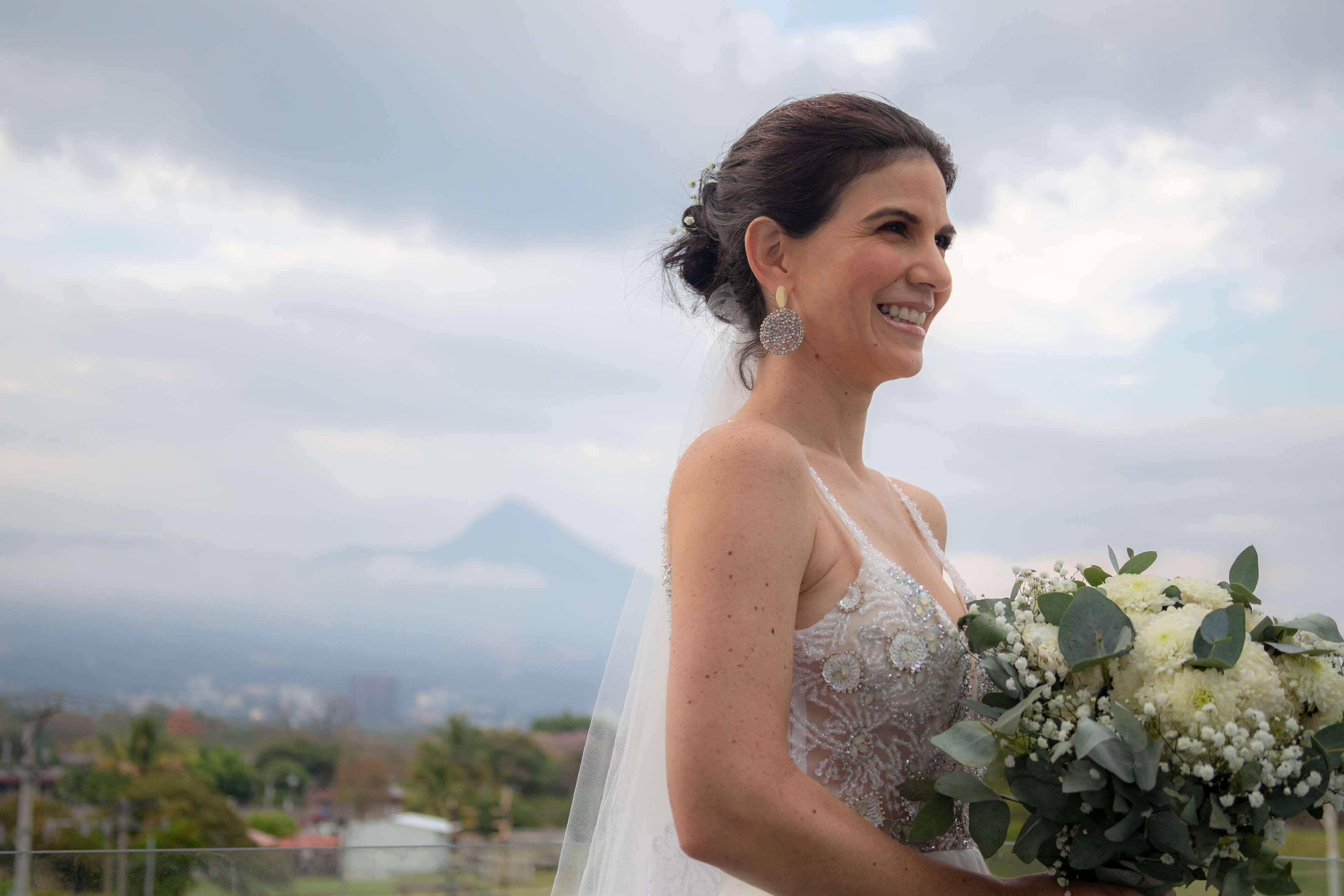A person in a wedding dress holding a bouquet, with a mountainous landscape in the background.
