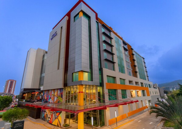 Um hotel moderno com uma placa destacada 'Hyatt Centric', entrada de vidro e um mural colorido na fachada.