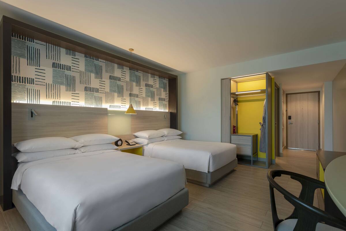 Une chambre d’hôtel avec deux lits, une table de chevet avec une lampe, un miroir et un petit bureau avec une chaise.