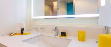 A modern bathroom with a white sink, a large mirror, and a yellow soap dish.