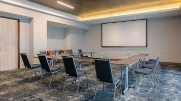 A conference room with a long table, chairs, a projector screen, and a carpeted floor.