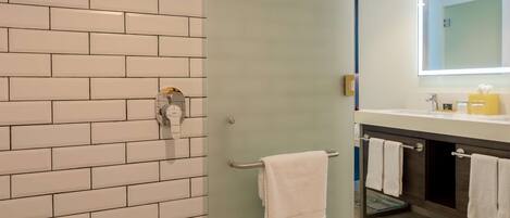 A bathroom with a tiled wall, a glass door, a patterned floor, and a mirror with a light.
