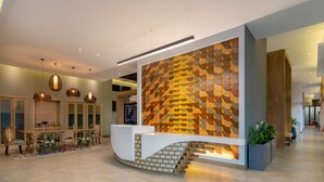 A modern reception area with a unique wooden wall design, a curved reception desk, and a staircase leading to an upper level. - Hyatt Centric San Salvador (Antiguo Cuscatlán)