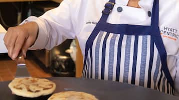 Een kok in een witte koksjas en gestreept schort bakt platbrood op een grillplaat.