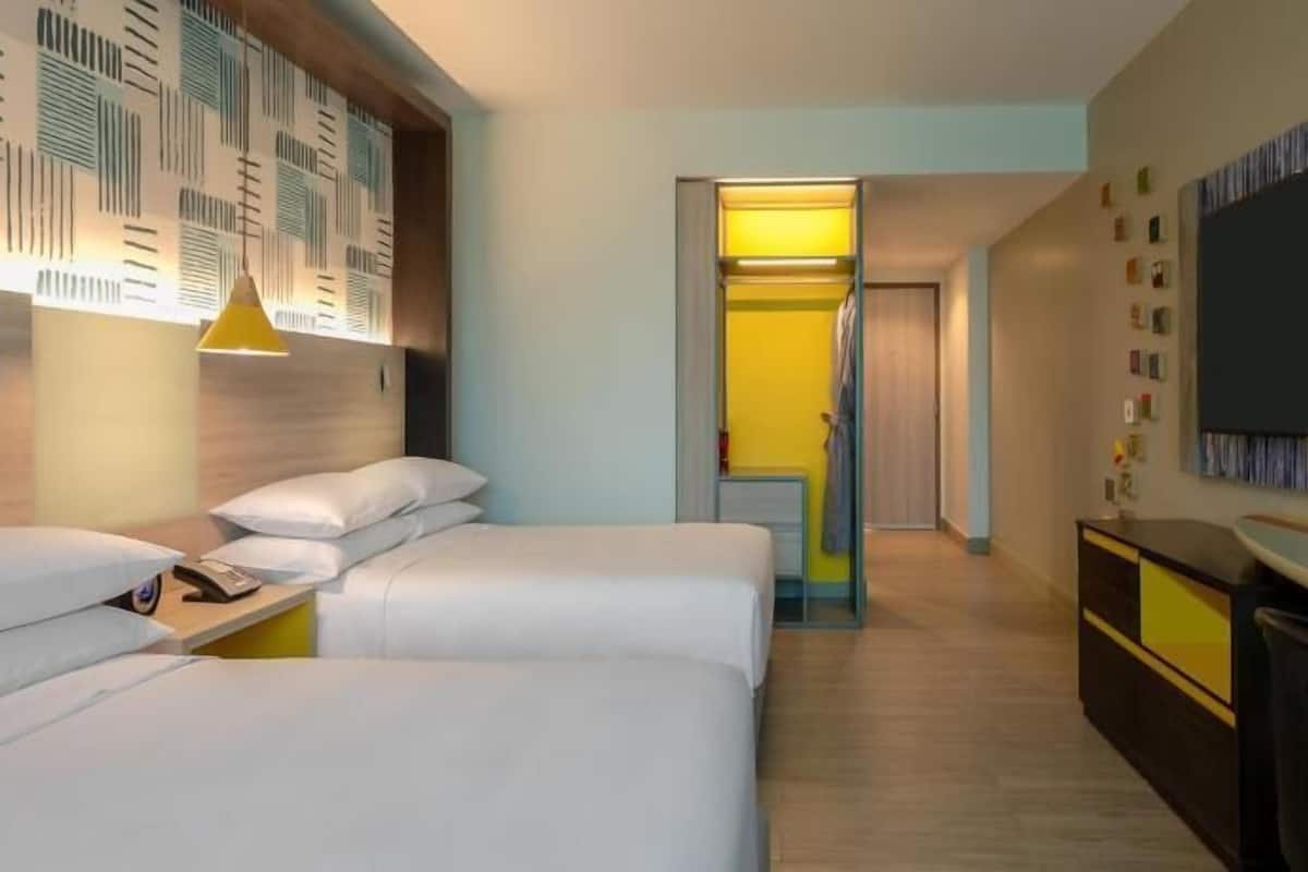 Une chambre d’hôtel avec un lit, une table de chevet, une lampe et un téléviseur fixé au mur.