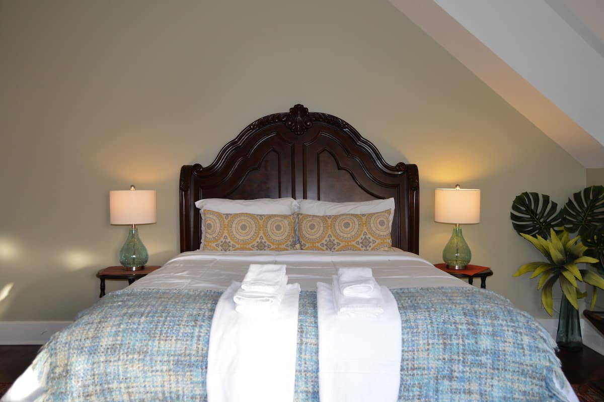 A neatly made bed with a patterned bedspread, two bedside lamps, and a potted plant.