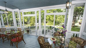 A covered outdoor area with glass tables and chairs, surrounded by white columns and large windows.