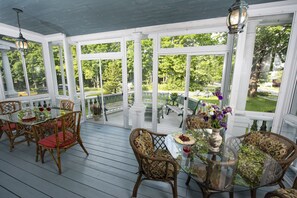 A covered outdoor area with glass tables and chairs, surrounded by white columns and large windows.