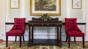 A room with two red upholstered chairs, a dark wooden console table with a vase of flowers, and framed artwork on the walls.