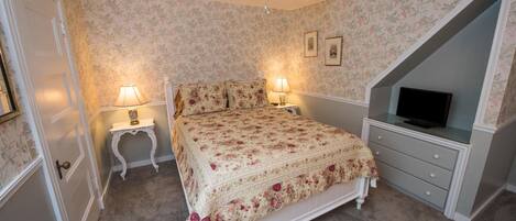 A bedroom with a bed, two bedside lamps, a television on a stand, and a ceiling fan.