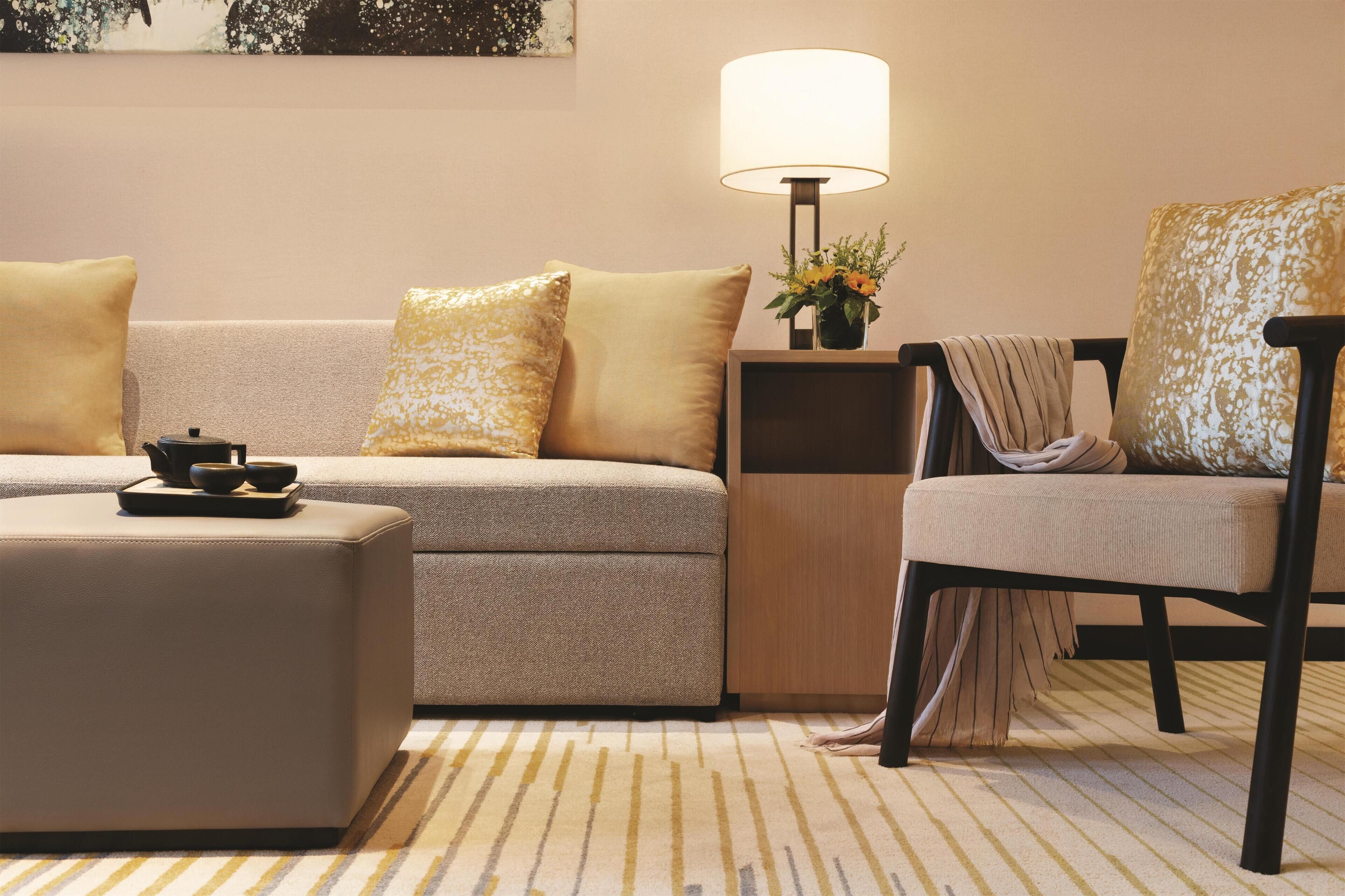 Una sala de estar moderna con un sofá, un reposapiés y un sillón, una lámpara y una mesita de centro con un arreglo floral.