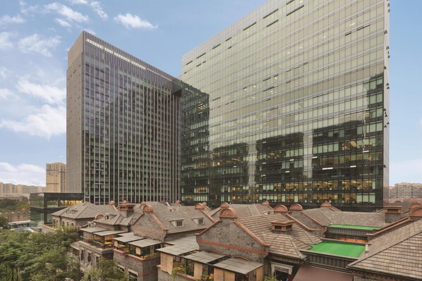 A modern high-rise building with reflective glass windows and a traditional low-rise structure with a green roof. - Hyatt Place Chengdu Pebble Walk (Chengdu)