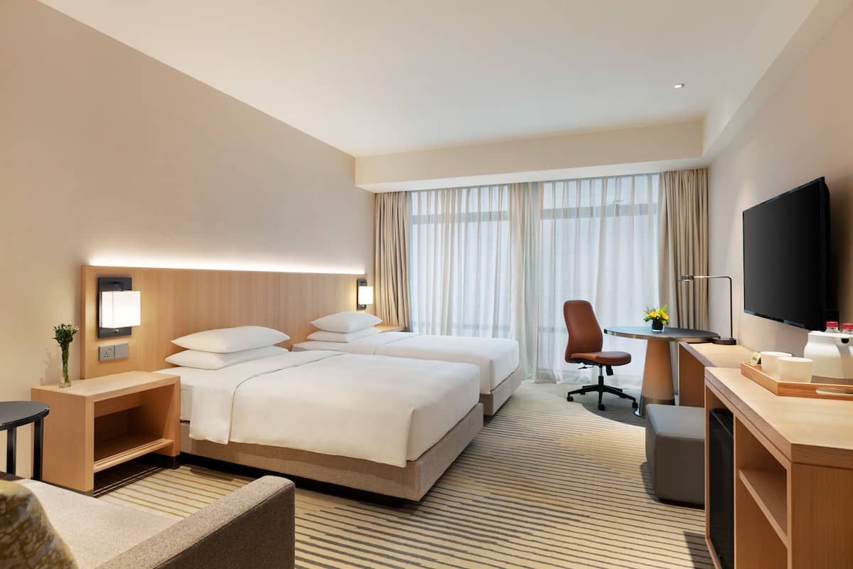 Quarto de hotel com duas camas, uma mesa, uma televisão e uma janela com cortinas.