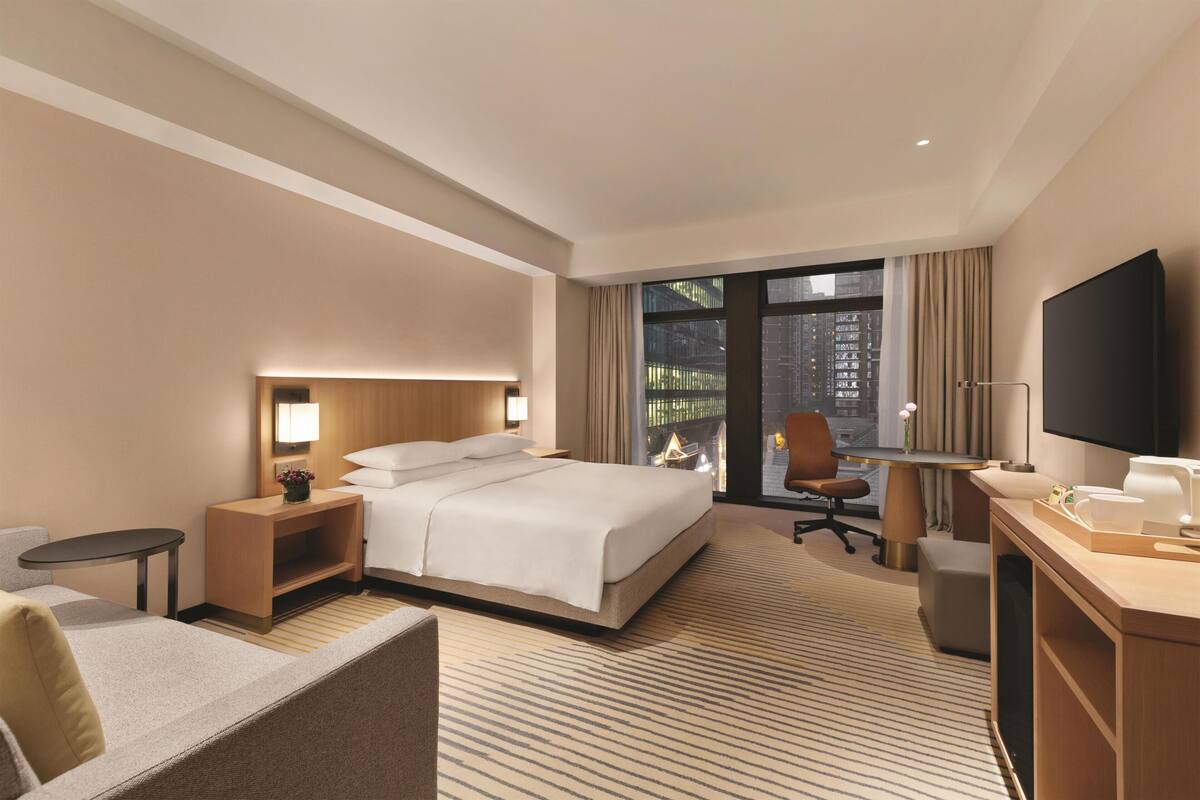 Quarto de hotel com cama, escrivaninha, cadeira, televisão e vista para a cidade.