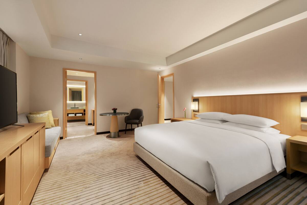 Quarto de hotel com uma cama grande, televisão, escrivaninha e uma cadeira.