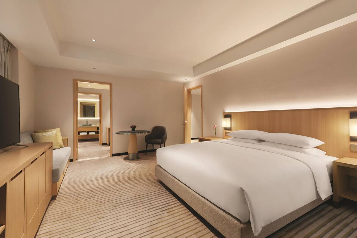 Quarto de hotel moderno com uma cama grande, uma escrivaninha, uma cadeira, uma televisão e um espelho.