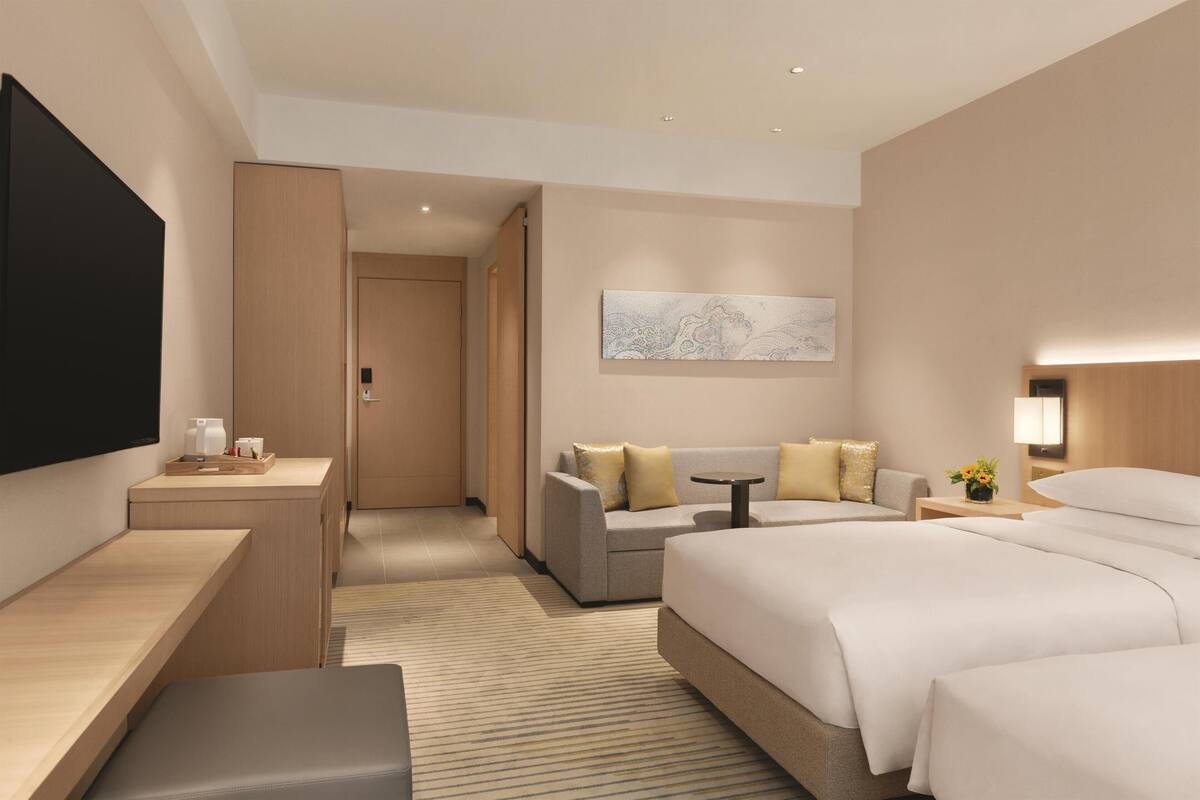 Quarto de hotel moderno com uma cama grande, um sofá, uma escrivaninha com uma televisão de tela plana e uma pequena mesa com abajur.